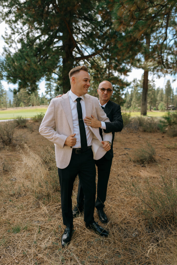 Another angle of the groom getting help with his jacket among rustic pine surroundings, captured during the Tahoe Mountain Club wedding day in Truckee.