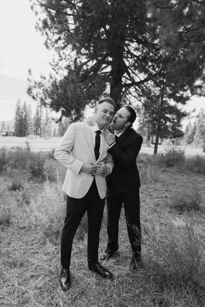 Black-and-white shot of a playful groomsman kissing the groom on the cheek, celebrating their Tahoe Mountain Club wedding in Truckee.
