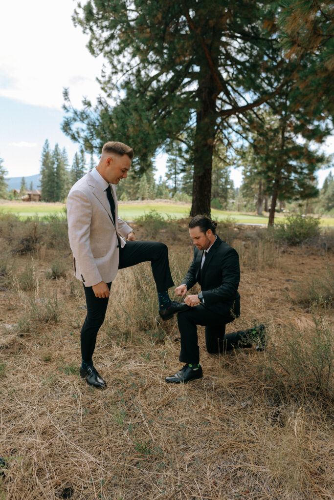 Groom playfully propping his foot while a groomsman ties his shoe, showcasing a lighthearted moment at a Tahoe Mountain Club ceremony.