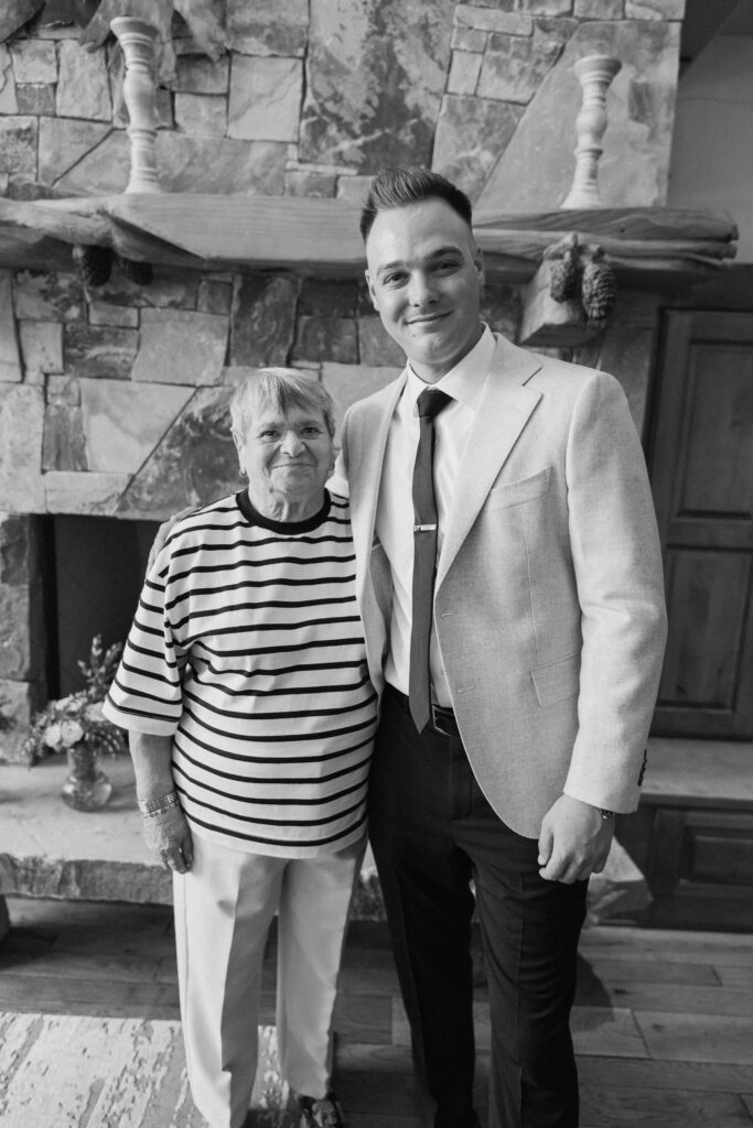 Groom with a family member in black-and-white by a stone fireplace, cherishing a quiet moment before the Tahoe Mountain Club wedding.