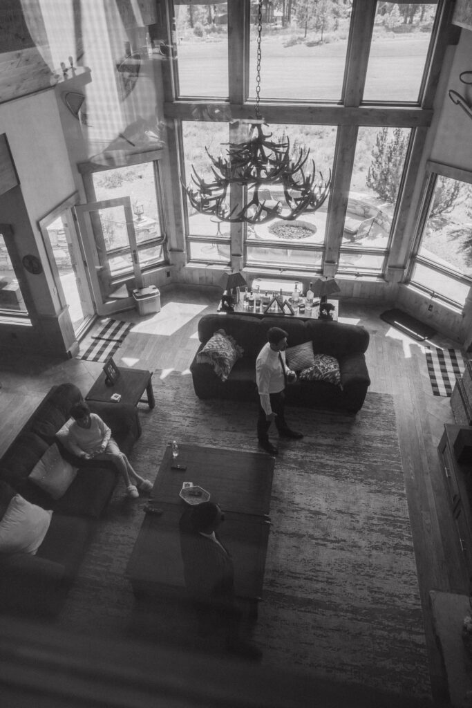 Overhead black-and-white view of a cozy living area with floor-to-ceiling windows, capturing the wedding party relaxing before a Tahoe Mountain Club ceremony.