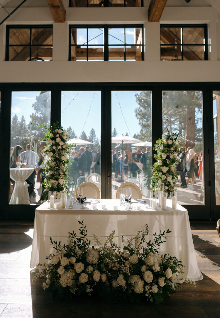 Sweetheart table at Tahoe Mountain Club wedding with tall white floral columns, rustic mountain décor, and large floor-to-ceiling windows.