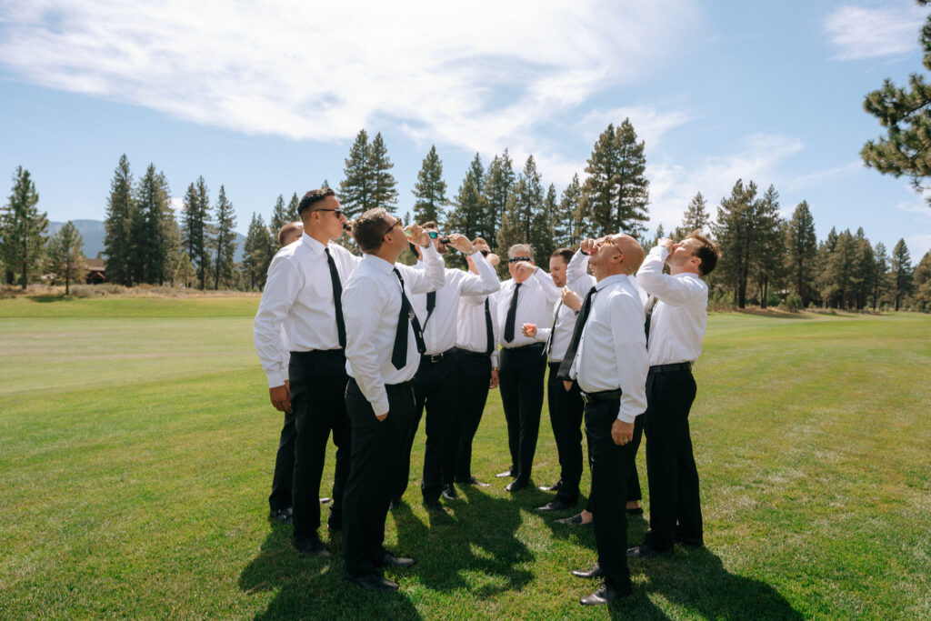 Groomsmen chatting and looking skyward on a sunny day, framed by pine trees at a Tahoe Mountain Club wedding celebration.