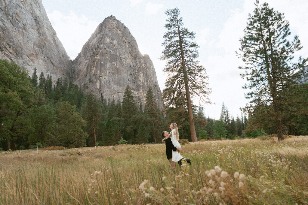 A whimsical moment with the couple dancing beneath rugged peaks in El Capitan Meadow, photographed by a Yosemite photographer.