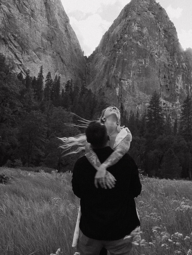 A black and white image of the couple gazing up at the towering cliffs near El Capitan Meadow, documented by a Yosemite photographer.