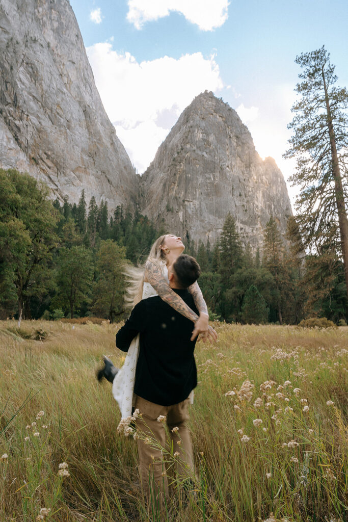 A couple spinning in the tall grasses of El Capitan Meadow with granite cliffs looming overhead, captured by a Yosemite photographer