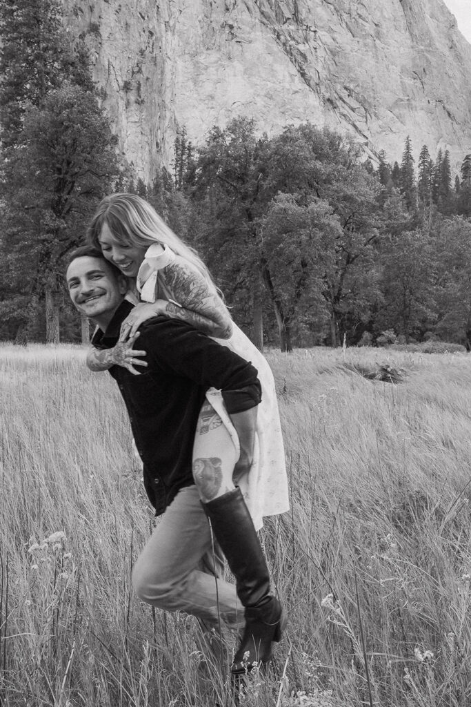 A black and white shot of a playful piggyback ride in El Capitan Meadow, photographed by a Yosemite photographer.