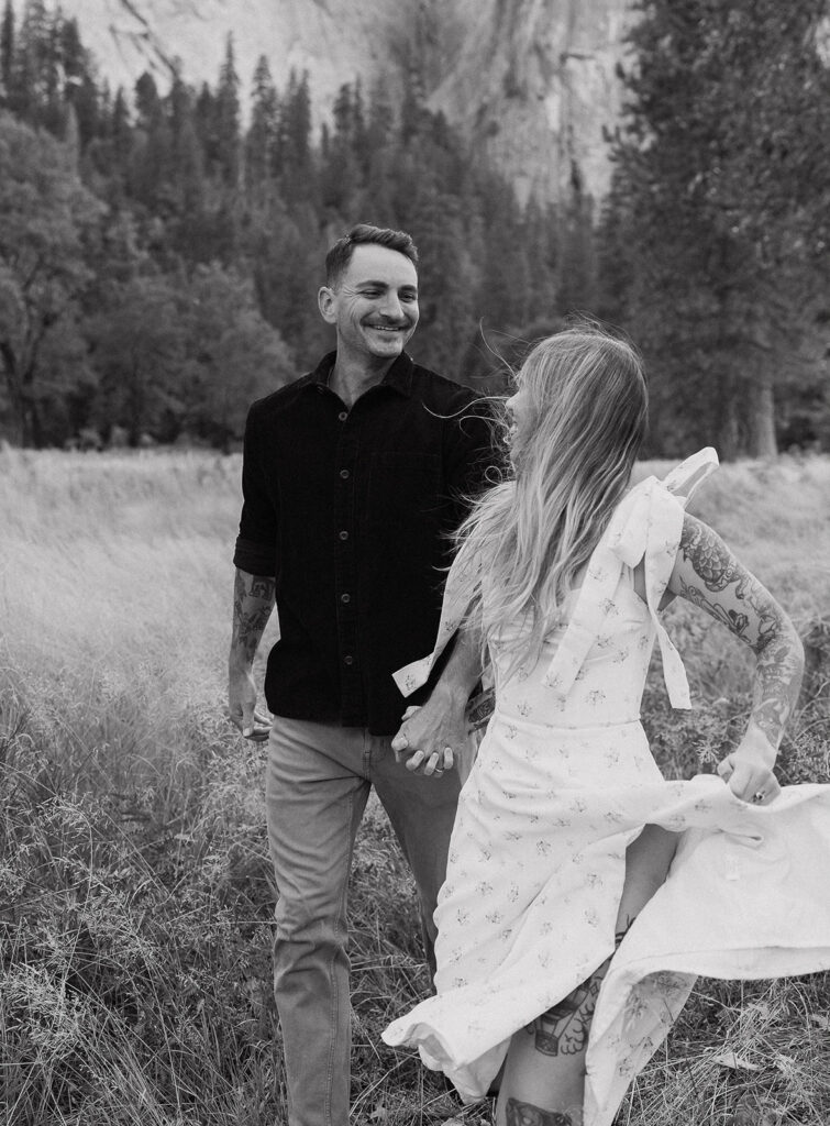 A black and white photo showing the couple laughing and strolling through El Capitan Meadow, taken by a Yosemite photographer